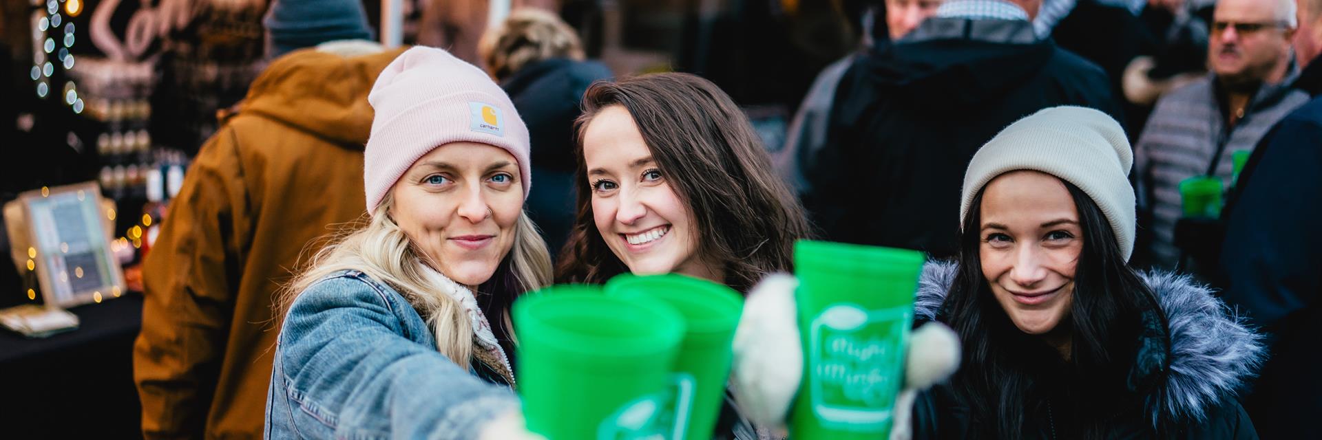 three women holding cups at holiday market